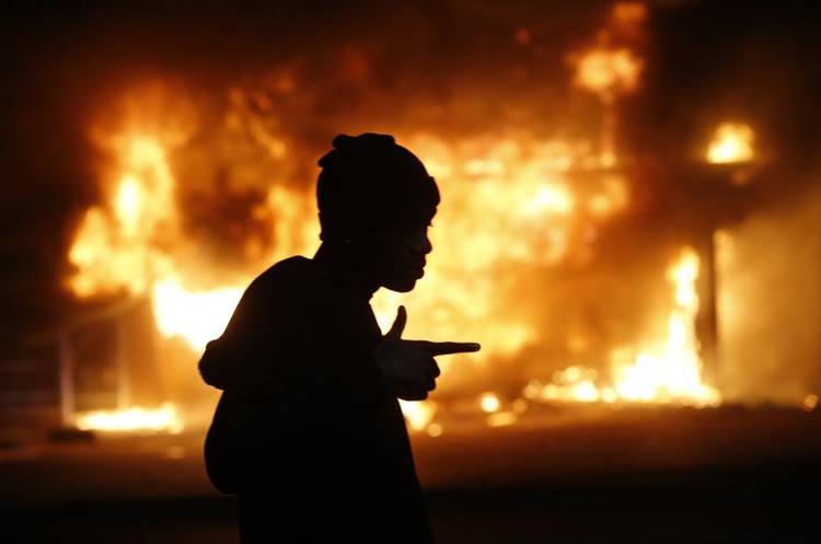 fot. Jim Young / Reuters / 25 listopada 2014  Ferguson, Stany Zjednoczone  Mężczyzna na tle płonącego budynku. Obiekt podpalono w trakcie zamieszek, które wybuchły po zastrzeleniu 18-letniego Michaela Browna w Ferguson. Sąd orzekł, że 28-letni policjant poprawnie wykonywał obowiązki służbowe.